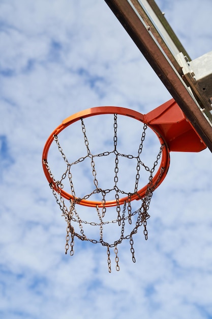 Ángulo bajo del aro de baloncesto con red de cadena colocada en el tablero sobre el fondo de un cielo azul nublado