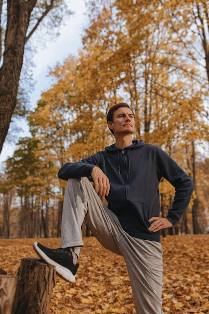 Ángulo bajo de deportista confiado estirando las piernas y entrenando en un día soleado en el parque en la temporada de otoño