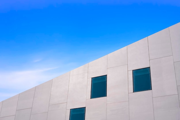 Ángulo bajo y vista lateral de las ventanas de vidrio en la pared de un edificio de hormigón blanco moderno contra el cielo azul