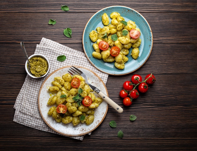 Nhoque em pratos com molho pesto verde, tomate e ervas em fundo de madeira rústico, close-up, vista superior. Prato tradicional da culinária italiana