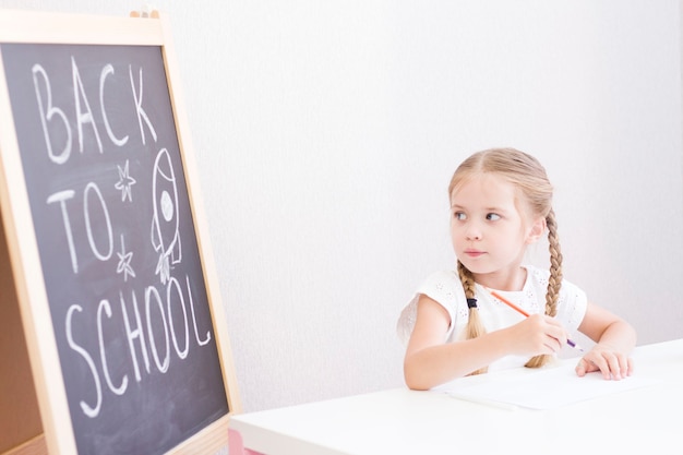 UNA NIÑA CON COLLOS ESTÁ SENTADA EN UN ESCRITORIO Y LEVANTA LA MANO. DE VUELTA A LA ESCUELA. ESCUELAS EN CASA