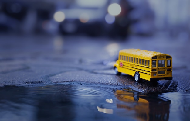 Ônibus escolar amarelo (modelo de brinquedo) durante a queda de chuva forte na cidade, vista de baixo ângulo e profundidade de composição de campo.