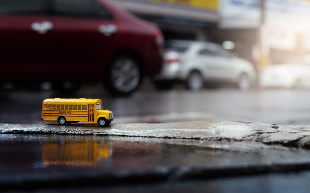 Ônibus escolar amarelo (modelo de brinquedo) durante a queda de chuva forte na cidade, vista de baixo ângulo e profundidade de composição de campo.