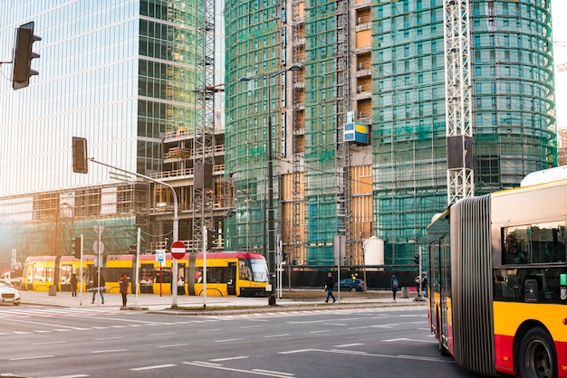 Ônibus público e bonde passam pelos modernos arranha-céus de vidro em construção.