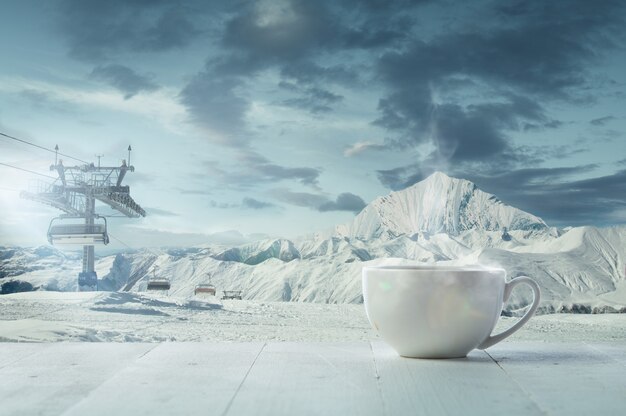 Única xícara de chá ou café e paisagem de montanhas no fundo. Xícara de bebida quente com aparência de neve e céu nublado na frente dela. Quente no dia de inverno, feriados, viagens, ano novo e época do Natal.