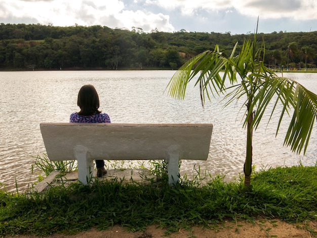 Nicht erkanntes Mädchen saß auf einem Sitz vor einem See in der Hintergrundbeleuchtung