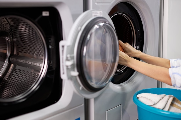 Nicht erkennbare Frau im Waschhaus, die saubere Kleidung sortiert, Haushaltsaufgaben erledigt, Frau zieht Kleidung aus der Waschmaschine heraus und hält Becken