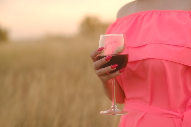 Nicht erkennbare Frau mit einem Glas Rotwein, die bei Sonnenuntergang in der Natur steht Körperteil der Frau in hellem Kleid mit Alkohol auf dem Land