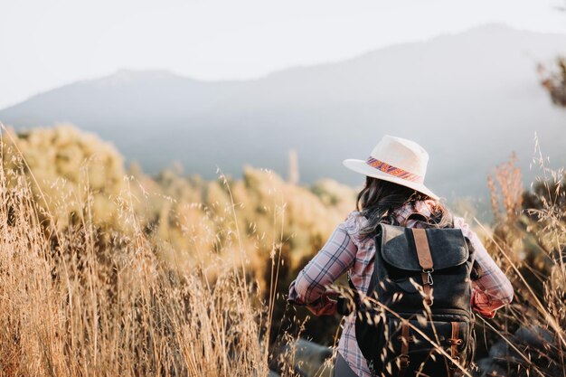 Nicht erkennbare Frau mit Hut und Rucksack beim Trekking durch das Feld