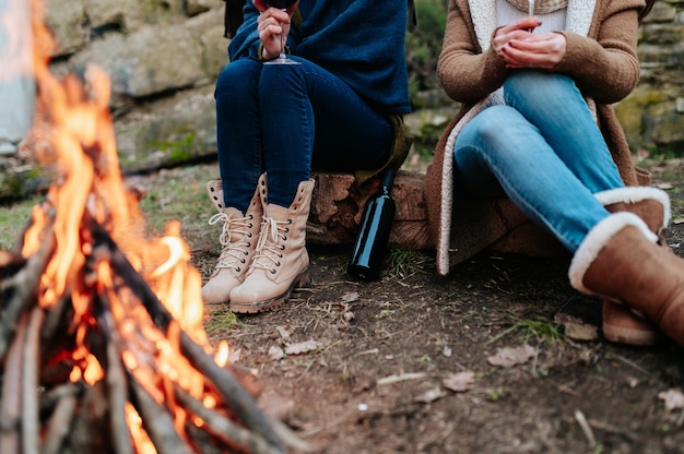 Nicht erkennbare Frauen, die ein Glas Rotwein am Lagerfeuer halten, das sich neben einem Feuer erwärmt.