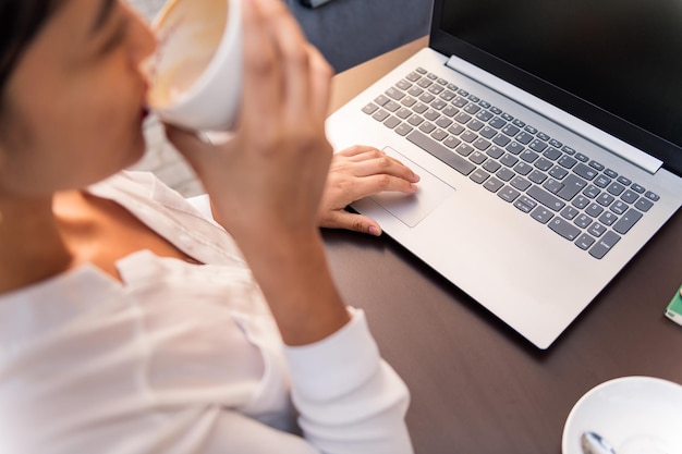 Nicht erkennbare Geschäftsfrau, die mit ihrem Computer arbeitet, während sie Kaffee auf einer Terrasse trinkt, Konzept des digitalen Unternehmers und des urbanen Lebensstils