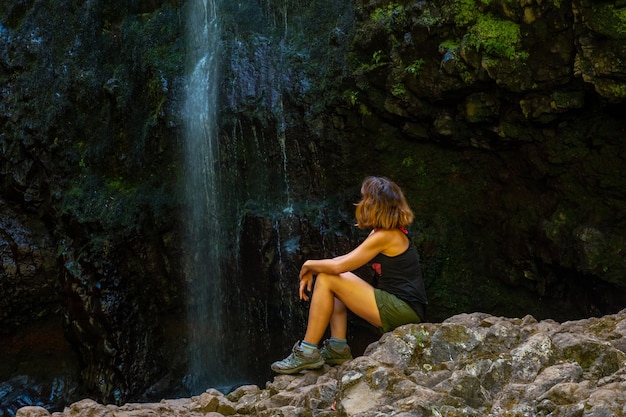 Nicht erkennbare junge Frau, die im Wasserfall an der Levada do Caldeirao Verde Queimadas Madeira sitzt