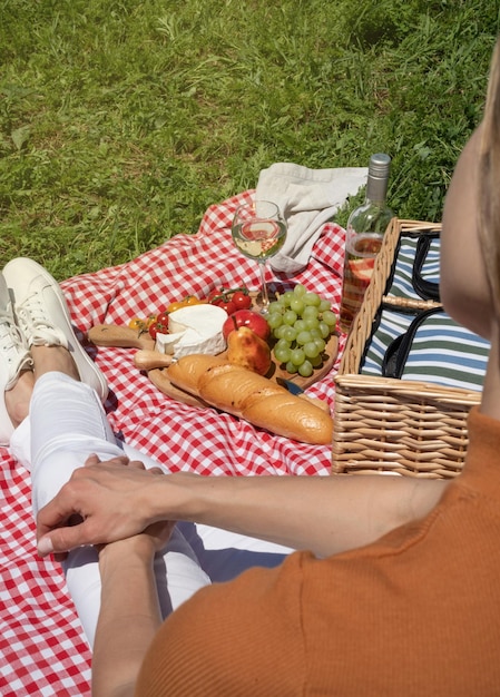 Nicht erkennbare junge Frau in weißen Hosen draußen, die Picknick essen und Gitarre spielen, Blick von hinten