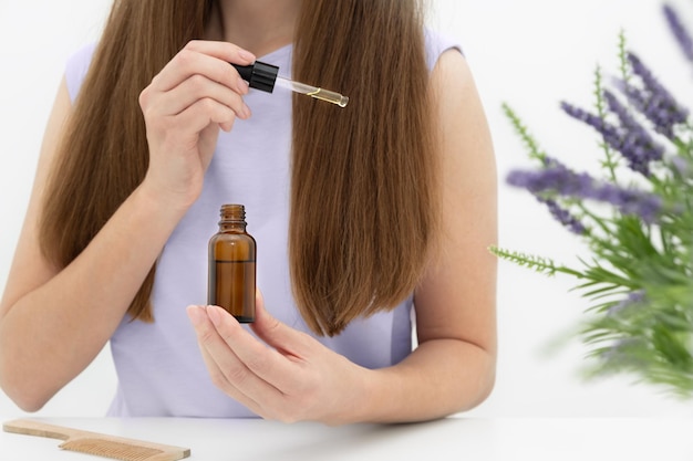 Nicht erkennbare kaukasische Frau mit langen braunen Haaren, die eine sehr peri-Bluse trägt, die eine Glasflasche sitzt und natürliches Serum auf das Haar aufträgt. Bio-Naturkosmetik, Schönheitsverfahren zu Hause Konzept, Nahaufnahme