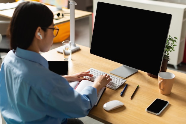 Nicht erkennbare Koreanerin, die Computer mit leerem Bildschirm im Büro benutzt