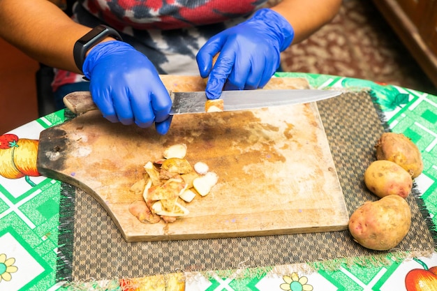 Nicht erkennbare lateinamerikanische Frau beim Kartoffelschälen mit blauen Handschuhen in ihrer Küche