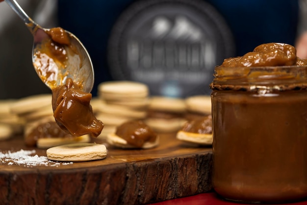 Nicht erkennbare Person, die Dulce de Leche aus dem Glas auf die Teigdeckel legt, um argentinischen Alfajor herzustellen