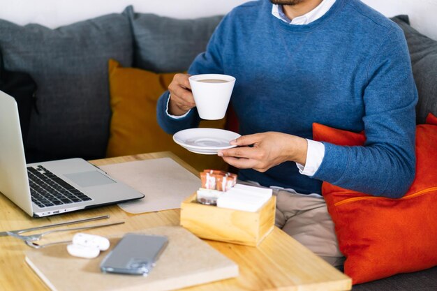 Nicht erkennbare Person in einem Café, die mit Telefon und Computer Kaffee trinkt.