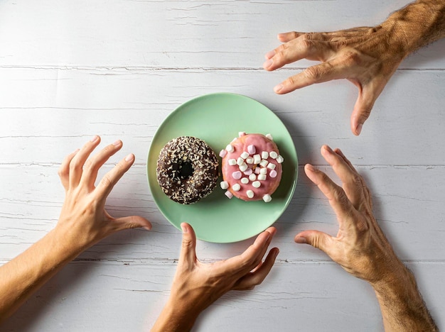 Nicht erkennbare Personen nehmen einen Donut von einem Teller auf einem Holztisch Draufsicht, Platzierung im Plan