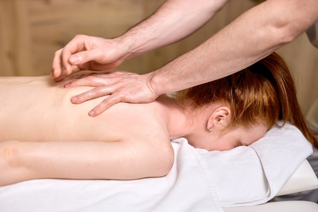 Nicht erkennbare rothaarige Frau, die Massage an der Wirbelsäule bekommt, Hautpflege, Spa-Konzept, Massage, Entspannung. im modernen Spa-Zentrum, Körpertherapie