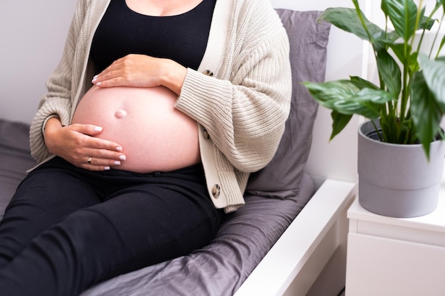 Nicht erkennbare schwangere Frau, die auf dem Bett liegt und zu Hause nackten Babybauch streichelt Happynatural Schwangerschaftspflege Entspannungskonzept