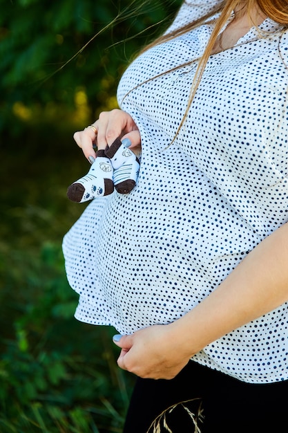 Nicht erkennbare schwangere Frau, die Bauch berührt und Babyschuhe hält