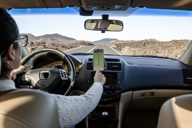 Nicht erkennbare weibliche Browsing-Karte auf dem Smartphone beim Fahren des Fahrzeugs auf der Straße in der Landschaft