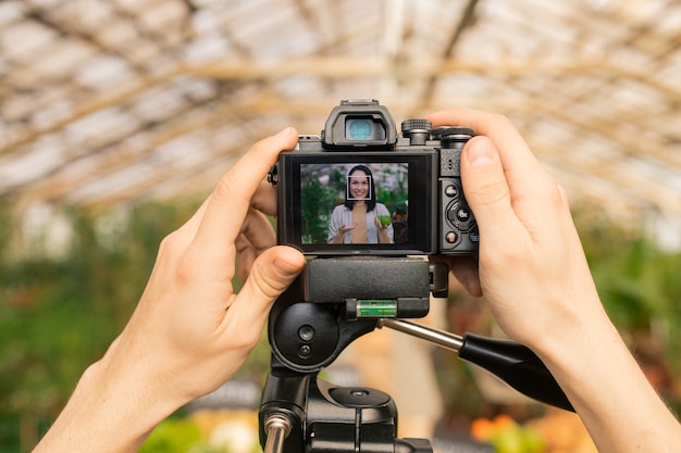 Nicht erkennbarer Bediener, der die Kamera für die Videoaufnahme des asiatischen Reformhaus-Bloggers im Treibhaus einstellt