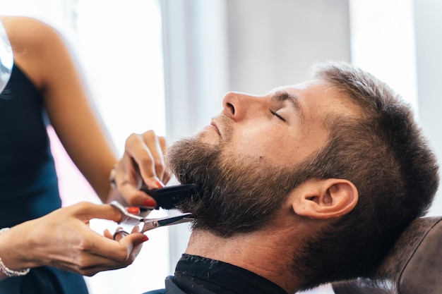 Nicht erkennbarer Friseur, der drinnen den Bart eines Mannes schneidet