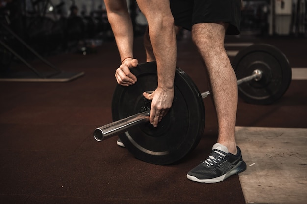 Nicht erkennbarer männlicher Athlet, der die Langhantel für sein Krafttraining im Fitnessstudio vorbereitet