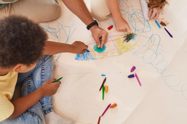 Foto nicht erkennbarer männlicher lehrer, der mit kindern arbeitet, die bilder zeichnen, während sie spaß in der vorschule oder im entwicklungszentrum haben