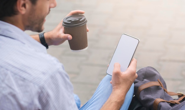 Nicht erkennbarer Mann, der draußen Kaffee trinkt und Smartphone benutzt