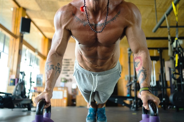 Nicht erkennbarer Mann, der Liegestütze mit Kettlebells in einem Fitnessstudio macht