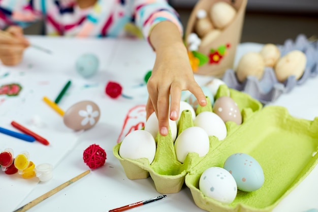 Nicht erkennbares kleines Mädchen nehmen Ei, malen, zeichnen mit Bürsteneiern zu Hause. Kind bereitet sich auf Ostern vor, hat Spaß und feiert Fest. Frohe Ostern, DIY