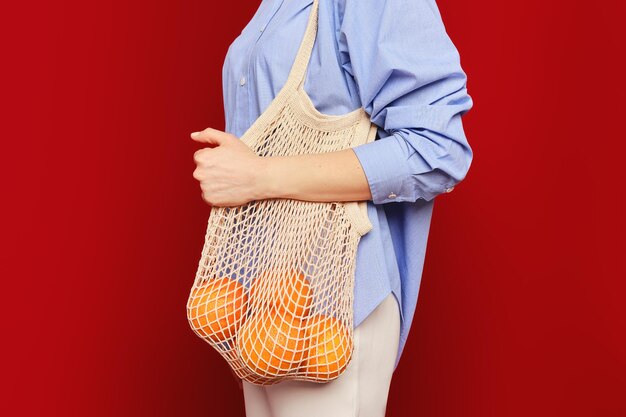 Foto nicht wiederzuerkennende frau hält orangen in einer einkaufstasche auf rubinrotem hintergrund