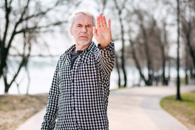 Nicht zulassen. Ernsthafter älterer Mann, der im Park steht und Hand zeigt