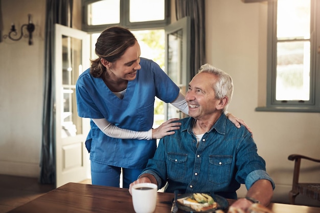 Nichts hebt meine Stimmung so sehr wie gutes Essen Aufnahme einer jungen Krankenschwester, die beim Frühstück in einem Pflegeheim nach einem älteren Mann sieht