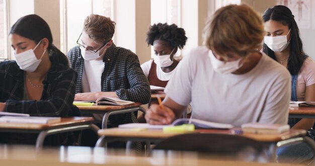 Nichts hindert sie daran, diese Note zu bekommen Foto von maskierten Teenagern, die in einem Klassenzimmer eine Prüfung schreiben