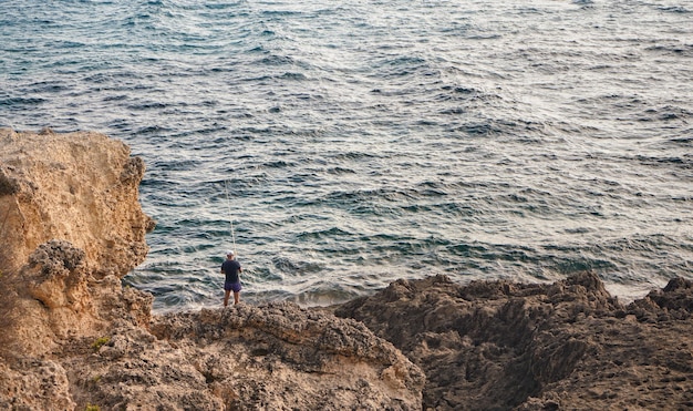 Único pescador em pé na costa rochosa do mar, vista por trás