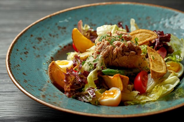 Nicoise-Salat mit Thunfisch und Kartoffeln in einem blauen Teller auf Holzhintergrund