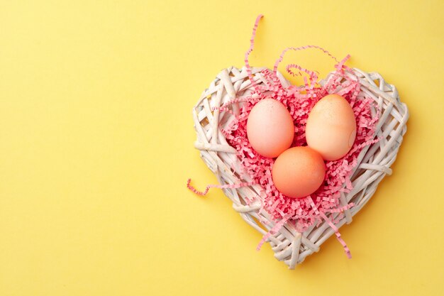 Nido decorativo con coloridos huevos de Pascua sobre fondo amarillo de cerca