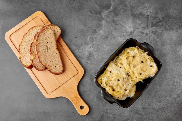 Nido de espaguetis relleno de filete de pollo con queso sobre un fondo de textura gris, junto a una placa de pan