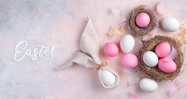 Nido de huevos de Pascua feliz y conejito de Pascua hecho de servilletas sobre un fondo rosa claro Vista superior