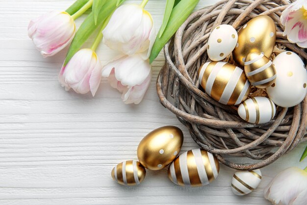 Nido con huevos de Pascua pintados de colores dorados sobre un fondo blanco de madera