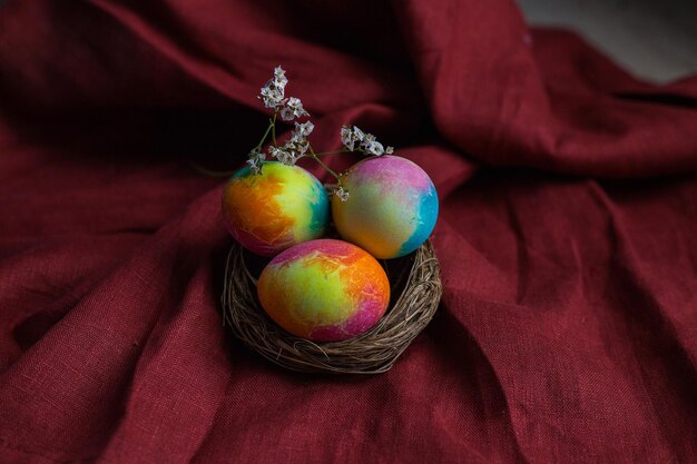 Un nido marrón con huevos pintados de varios colores sobre un fondo de tela burdeos Decoración de Pascua Decoración de Pascua de primavera