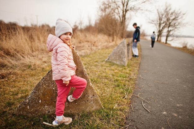 Niedliche Babymädchen tragen eine rosa Jacke am Ufer des Sees