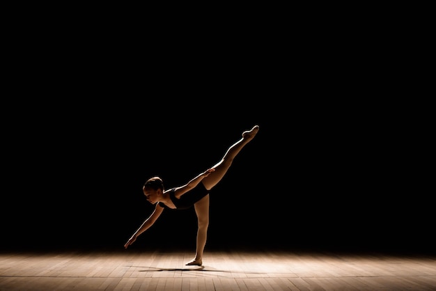 Niedliche kleine Ballerina im dunklen Ballettkostüm, das auf der Bühne tanzt. Kind im Tanzkurs. Kind Mädchen studiert Ballett.