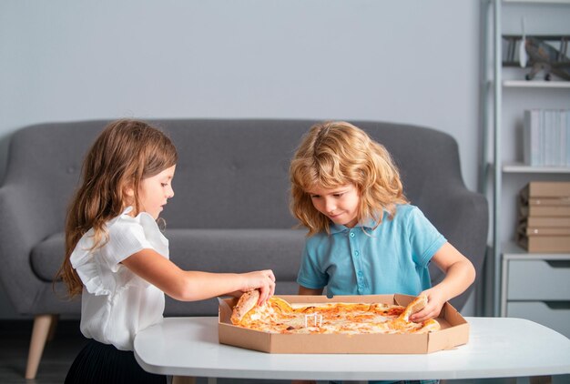 Niedliche kleine Jungen und Mädchen, die zu Hause Pizza essen. Kinder halten ein Stück Pizza auf einer Party zu Hause