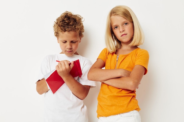 Niedliche, stilvolle Kinder stehen neben einem Notizblock, der Emotionen mit unverändertem Farbhintergrund zeichnet. Foto in hoher Qualität