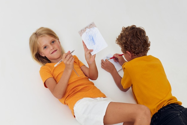 Niedliche Vorschulkinder Emotionen zeichnen zusammen Notizblock und Bleistifte hellen Hintergrund unverändert